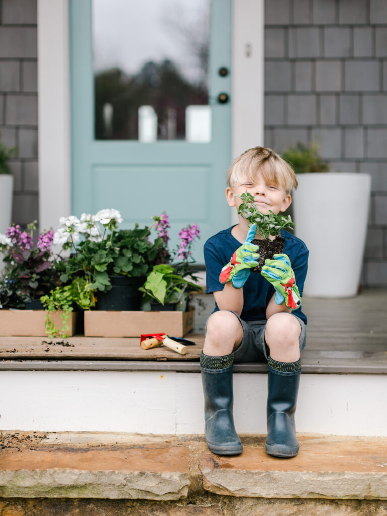 A young boy sitting on the steps of a Mayfair home holding a plant in New Braunfels.