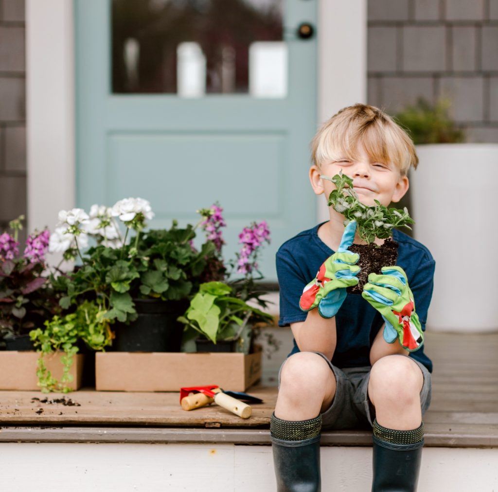 A young boy sits on the steps of a Mayfair home holding a plant.