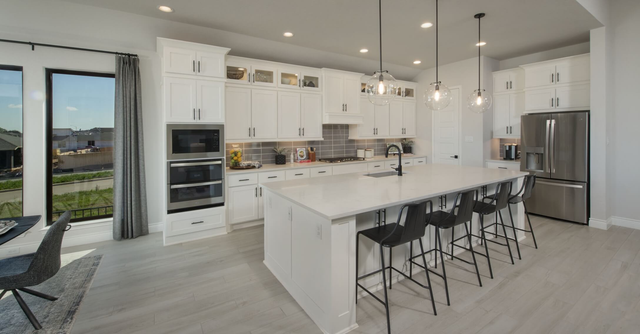 A white kitchen with stainless steel appliances and bar stools in new homes in New Braunfels Texas.