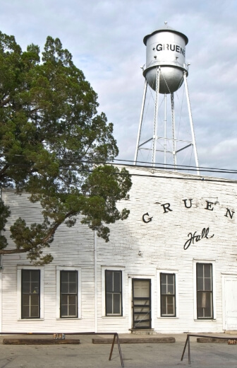 A white building with a water tower in the background, located amongst parks and trails in New Braunfels, Texas.