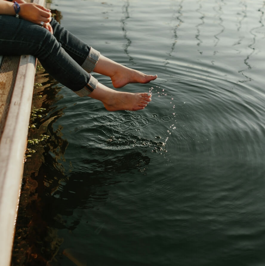 A woman is sitting on a dock with her feet in the water.