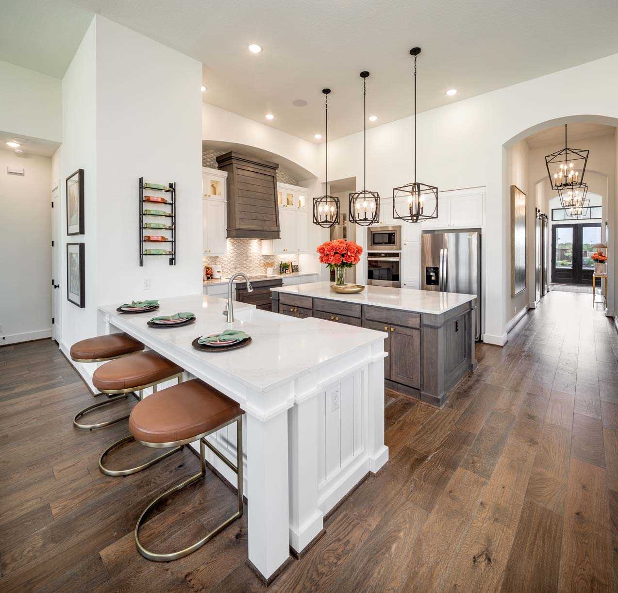 Modern kitchen interior in New Braunfels with a central island, bar stools, stainless steel appliances, and pendant lighting.