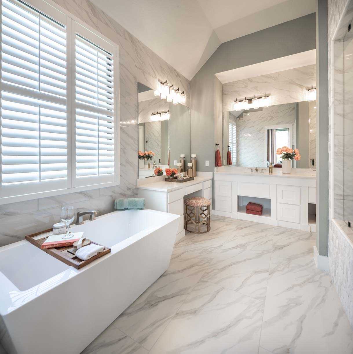 Spacious modern bathroom in a new home with marble finishes, featuring a freestanding tub, dual sink vanity, and large windows with shutters.