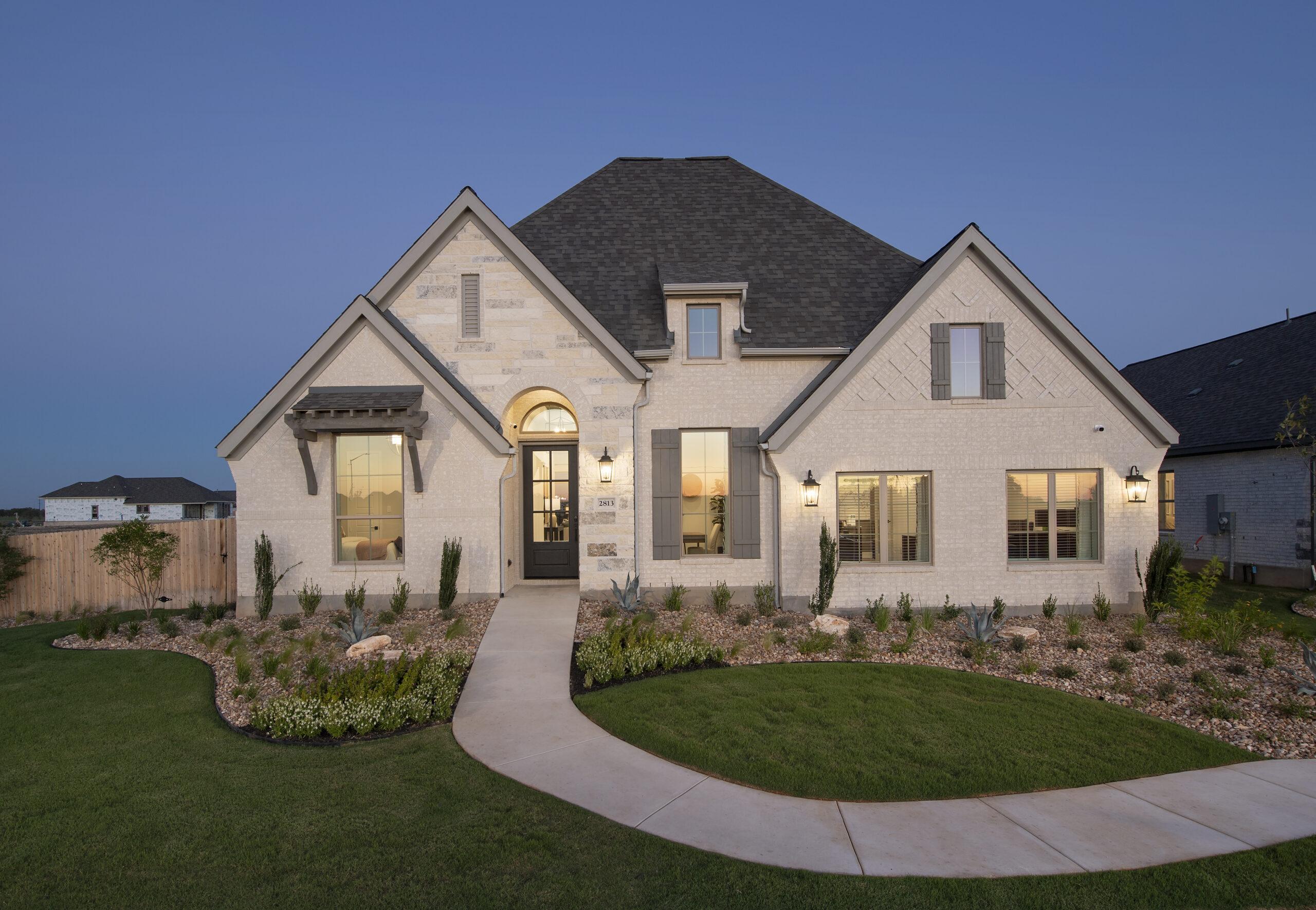 A single-story suburban house in New Braunfels with exterior lighting on at dusk.