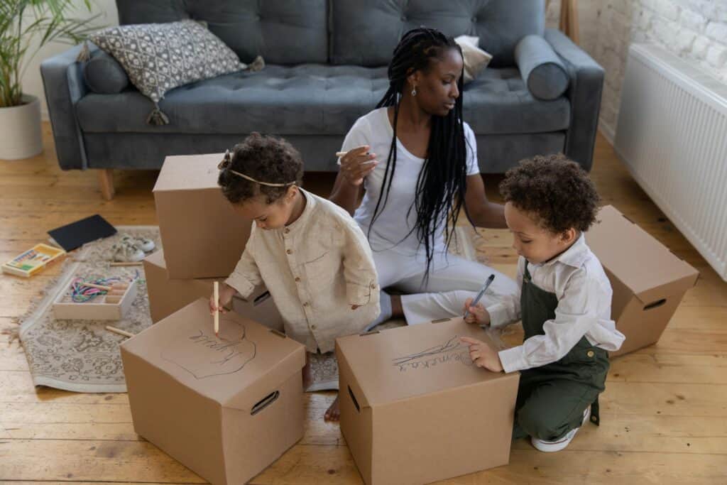 Woman packing moving boxes with two young toddlers coloring on the moving boxes with markers. Moving to New Braunfels? Moving Resources Checklist