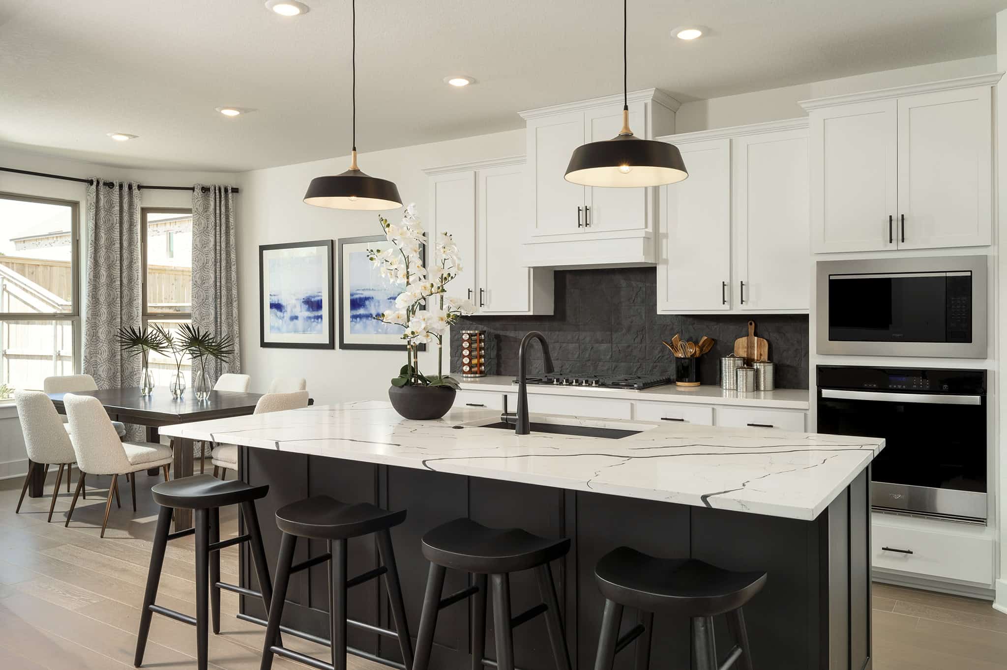 Modern and beautifully designed kitchen with two hanging pendant lights, a white granite countertop, and four black stools behind the long kitchen island.