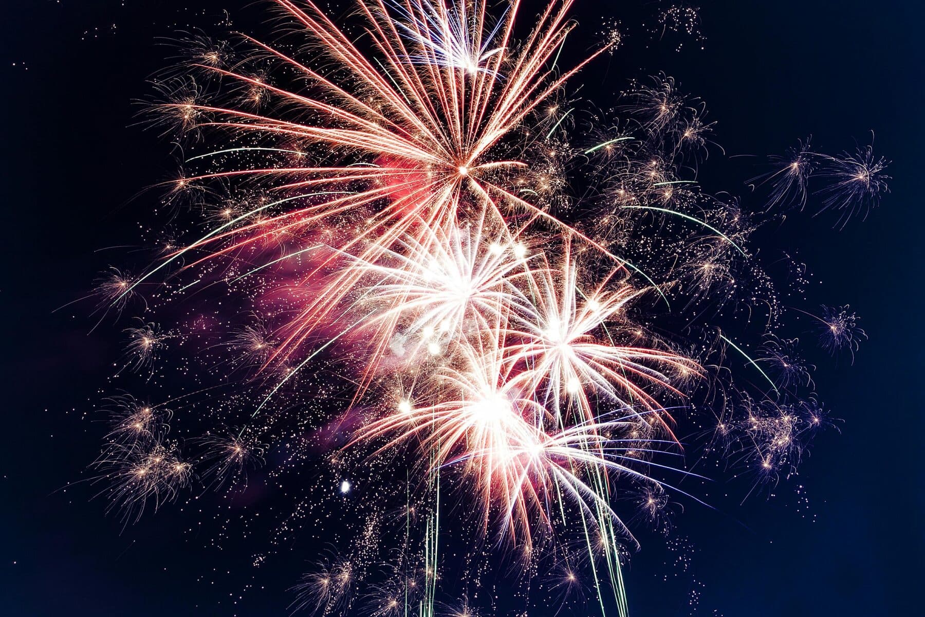 Bright, colorful fireworks burst against a dark night sky, with sparks and trails radiating outward in multiple directions.
