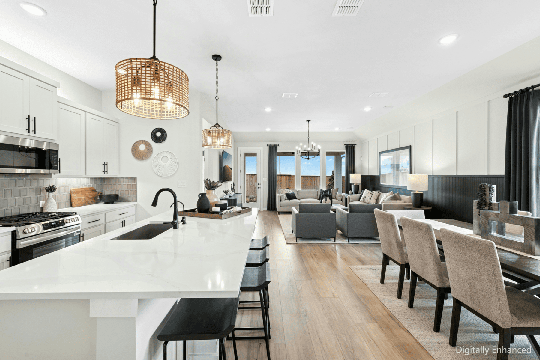 Open-concept kitchen, dining, and living area with modern furnishings, white cabinetry, pendant lighting, and large windows letting in natural light.