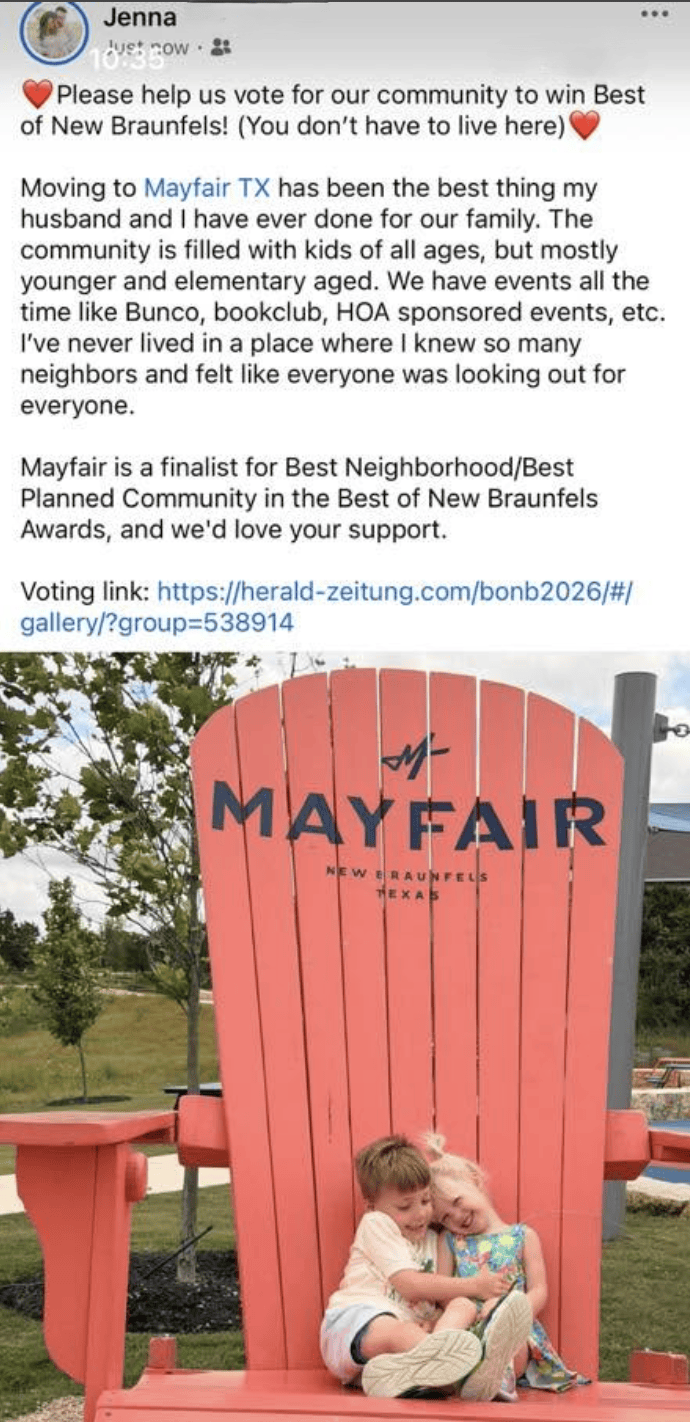 Two young children sit together smiling on a giant red chair outdoors with the word "MAYFAIR" and a logo above them.